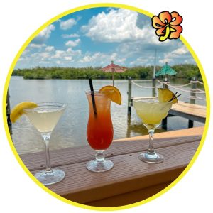 Three cocktails are sitting on a table near the water.